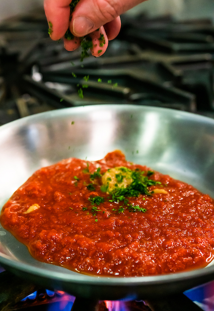 Red pasta sauce garnished with herbs on a stove top